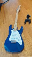 Blue electric guitar laid on hardwood floor with black wall mount visible to right