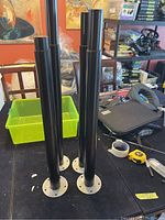 Four black IKEA OLOV adjustable table legs standing upright showing full length and silver base.