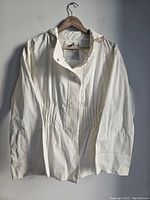 Full front view of white Moncler ladies jacket with visible front details and hood, on wooden hanger against white wall.