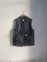 Front view of black Carhartt vest hanging showing zipper and pockets