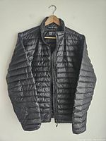 Front view of the black MEC down jacket hanging on a hanger shows full front, zipper closed, sleeves and collar.