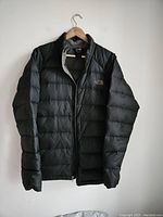 Front view of the men's black down jacket by The North Face hanging on a hanger.
