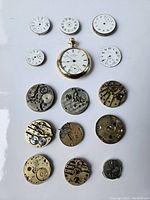 Layout of 15 items including one Waltham pocket watch, five watch dials, and multiple mechanical watch movement parts on white background.