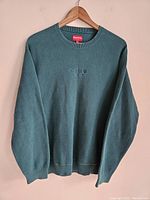 Front view of the green Supreme sweatshirt hanging on wooden hanger showing embroidered logo.
