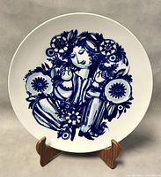 Front view of the 13 inch white porcelain wall plate with blue artistic design of a woman and flowers.