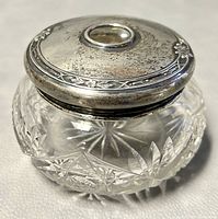 Oblique angle photo showing sterling silver lid on cut crystal bowl, highlighting tarnish and dents on lid and pinwheel crystal pattern.