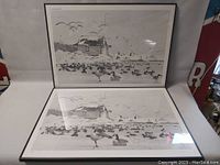 Two framed prints with a coastal scene featuring birds and a building near the water displayed upright.