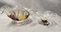 Two vintage footed serving bowls displayed side by side on a neutral backdrop, one larger and clear glass, the other smaller with a silver-tone footed base.