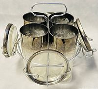 Set of four silver lustreware highball tumblers arranged in a stainless steel caddy with four matching coasters attached.