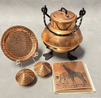 Photo showing entire copperware lot with footed covered pot, small hammered plate, salt and pepper shakers, and six coasters with giraffe design.