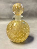 Front view of the round Murano blown glass perfume bottle showing golden dotted pattern and the spherical ribbed stopper with vertical gold flecks.