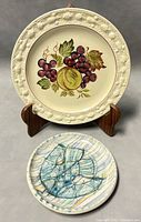 Front of two plates: one large decorative fruit plate and one smaller abstract design plate.