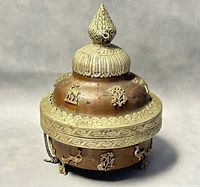 View of the copper container with mixed metal decorative lid, showing intricate claw feet and embossed ornamental designs.