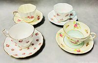 Four different teacup and saucer pairs arranged showing floral patterns, rims, and shapes