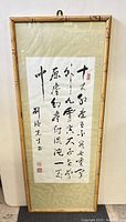 Full view of framed Chinese calligraphy wall art held vertically showing bamboo-style frame, fabric mount, and sealed calligraphy piece.