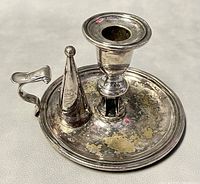 Photo of the metal hand candleholder with handle and snuffer, showing peeling and dents on the surface.
