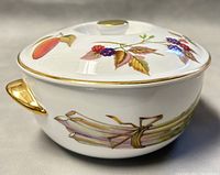 Side view of Royal Worcester EVESHAM oval covered baking dish showing blackberry and asparagus botanical design with gold-toned handle and rim accents.