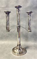 Front view of vintage 3-arm stainless steel candelabra standing on a grey surface with a grey background