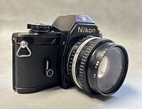 Front left angle view of Nikon EM camera with attached 50mm Series E lens showing body and lens details.