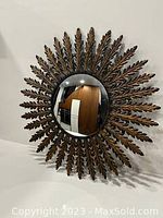 Front angled view of concave mirror with metal starburst frame showing leaf details and reflective surface
