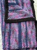 Detail view of the folded blanket showing thick knit texture, slate blue, dusty mauve, dusty pink melange colors and black border.