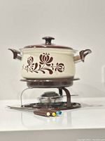 Full view of enamel fondue pot on stand with burner and fondue forks placed in front