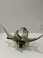 Side view of olive green MCM glass art sculpture showing flowing abstract form with pointed ends and curved shapes.