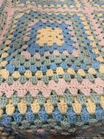 Close-up of corner showing hand crocheted granny square pattern in pastel colors aqua green, blue, yellow, and cream with soft pink joining.