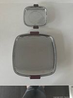 Small and large square stainless steel trays with bakelite handles and feet, viewed from above on white surface
