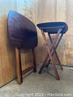 Two walnut folding tables, one folded flat against wood-paneled wall, other standing open, showing foldable leg design and wood grain finish.