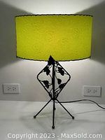 Front view of lamp showing green textured fabric shade and wrought iron base with leaf decorations