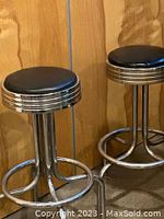 Pair of vintage heavy metal bar stools with black vinyl seats and chrome bases, showing overall condition and style