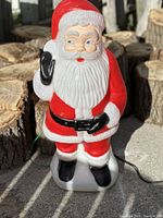 Front view of blow mold Santa Claus figurine standing upright outdoors on concrete with wood background.