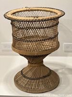 Full view of the vintage plant stand showing the round top, woven wicker body with black banding details and the flared base.