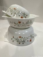 Stacked view of the three Emily Spring Garden white glass casseroles or nesting bowls showing floral decoration and handles.