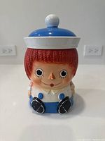 Front view of vintage Raggedy Andy ceramic cookie jar showing facial details, hat lid, and painted features.