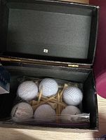 Photo of a black box with six white golf balls and wooden golf tees inside.