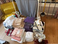 Overview photo showing a variety of folded towels, a purple bath pillow, a fabric laundry hamper, a folding basket, and a box with appliances and accessories.