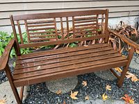 Front view of wooden garden bench outside on gravel with plants in background.