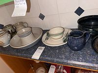 Various ceramic serveware pieces displayed on a kitchen countertop including pitchers, bowls, a large serving bowl, and a platter with leaf decoration.
