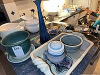 Photo showing assortment of ceramic serveware including tall blue vase, green planter, small bowls, and plates laid on a tray