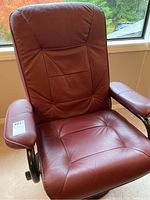 Front view of a red leather and man-made material recliner chair with padded armrests and detailed tufted stitching.