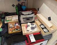 Overall view of the lot showing various containers, bags, recipe box, two wooden boxed weather instruments, and napkin.