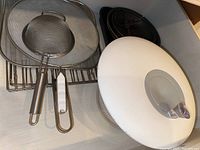 Top view of assorted cookware including mesh splatter guard, stainless steel utensils, and wire racks.