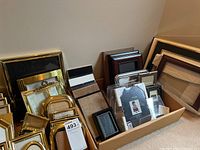 Photo showing multiple stacked frames including gold-tone metal and dark wood against the wall and floor.