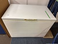Closed rectangular white chest freezer from front view showing label and control panel on lid.
