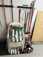 Four plastic patio chairs stacked with striped cushions and wrapped in plastic, gardening gloves and various accessories placed in front