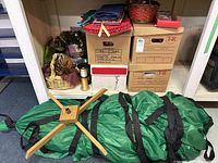 Overview of boxed holiday decorations, artificial Christmas tree in green bags, red basket, and assorted fabric pieces on shelf