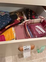 Drawer containing a variety of kitchen linens including folded towels, trivets, placemats, and a pink silicone oven mitt.