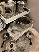 Multiple stainless steel pots and pans with lids on two sliding shelves. Includes pressure cooker with locking handle.